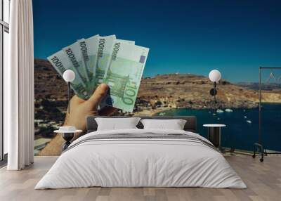 Man holds money against the backdrop of a beach in a warm country. Wall mural