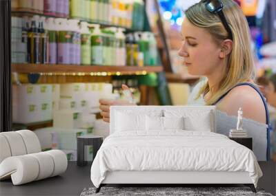 Young woman choosing cosmetic cream in beauty shop. Wall mural