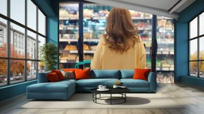 Back view of woman shopping for frozen food in front of refrigerator in supermarket Wall mural