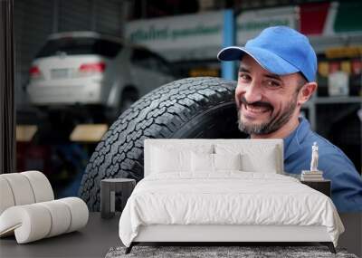 Male mechanic with car tire in auto store, Specialist tire fitting in the car service, checks the tire and rubber tread for safety Wall mural