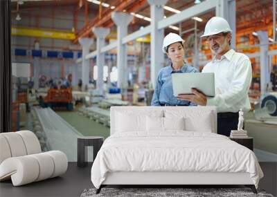 Two professional engineer man and woman manager leader wearing helmet and holding laptop standing in factory talking and discussing for work Wall mural