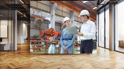 Two professional engineer man and woman manager leader wearing helmet and holding laptop walking in factory talking and discussing for work Wall mural