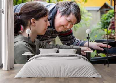 a caregiver explains to a mentally disabled woman how to plant zucchini in a bucket Wall mural