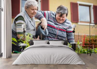 senior mother and her mentally disabled daughter watering plants together with a watering can Wall mural