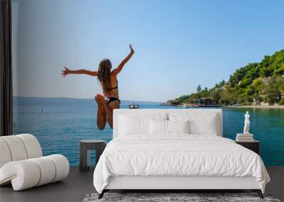 Happy young female jumping into water- vacation, freedom, travel destination concept Wall mural