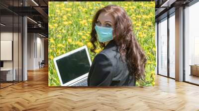 A woman in a business suit in a sterile medical mask on her face. looking at the camera with a laptop computer
Young freelancer working in the park. Dandelions field. Virus, pandemic coronavirus conce Wall mural