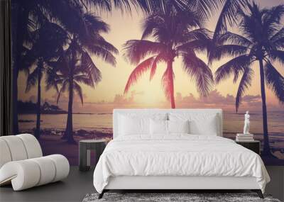 Tropical beach with silhouettes of coconut palm trees at sunset, color toning applied. Wall mural