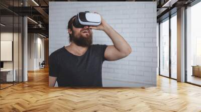 Bearded male hipster looking shocked with his mouth open, wearing virtual reality glasses, copy space. Young man using vr 3d glasses at work. Man trying vr headset. Innovations, technology, digital co Wall mural