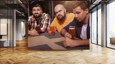 Group of male friends looking upset, drinking beer after watching football game. Three men unhappy after the loss of their favourite team, drinking at beer pub Wall mural