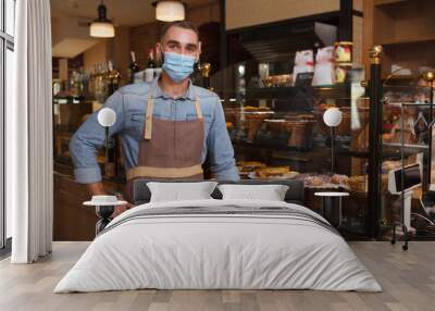 Male baker wearing medical face mask working at his bakery store during coronavirus quarantine Wall mural