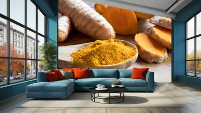 Turmeric powder on a wooden spoon, with turmeric root in the background Wall mural