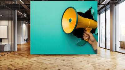 Human hand holding a yellow megaphone through a hole in blue paper Wall mural