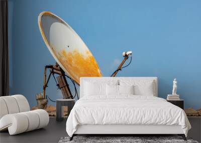 Old rusty satellite dish antenna on a tiled roof against blue sky Wall mural