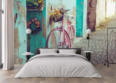 Pink vintage bike with basket full of flowers next to an old cyan building in Spain Wall mural