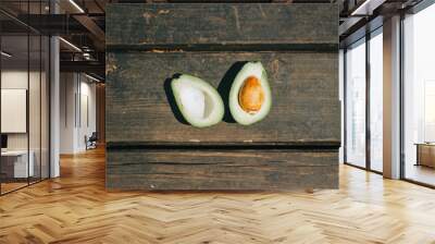 Top view of a single avocado cut in half with brown seed on dark wooden planks – Health exotic fruit placed on a brown surface – Fresh snack for a nutritious diet Wall mural