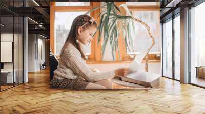 Beautiful 9 year old brunette girl reading a big book and smiling within a shiny bright room Wall mural