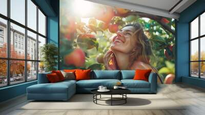 A woman laughing while picking apples in an orchard, the trees laden with ripe fruit, with sunlight filtering through the leaves, creating a scene of simple joy and abundance Wall mural