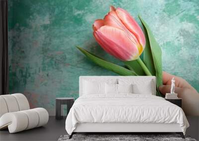 Hand holding a pink tulip, on a green background, bright light, top view 2 Wall mural