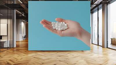 Hand holding white round pills, on a light blue background, natural light, close-up view 3 Wall mural