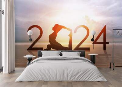 Happy new year card 2024. Silhouette of healthy girl doing Yoga One Legged Pigeon pose on tropical beach with sunset sky background, woman practicing yoga as a part of the Number 2024 sign. Wall mural