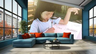 Little Asian girl love to drawing mermaids and angles on sketchbook with black pen, sitting on terrace beside exotic island, mataking island, Malaysia, children art Wall mural