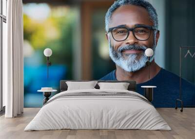 Portrait of a joyful relaxed man wearing glasses standing in the warm indoor sunlight and having a peaceful content smile on his face  Capturing a moment of calm and happiness in a simple Wall mural