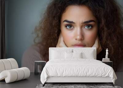 Portrait of a young woman with curly hair sitting hunched on a chair hands resting on her belly showing signs of discomfort distress or digestive upset such as abdominal pain or gastritis Wall mural