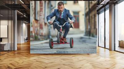 A man in a business suit rides a small red tricycle, showing a juxtaposition of fun and professionalism in an urban setting Wall mural