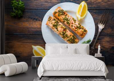 Salmon roasted in an oven with a butter, parsley and garlic. Portion of cooked fish and fresh lemon on a white plate on the wooden background, top view. Wall mural