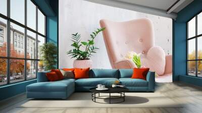 Stylish pink armchair with heart shaped pillow in a bright minimalist interior. Wooden shelving unit with decor near grey wall. Bookcase with candles, living room interior details Wall mural