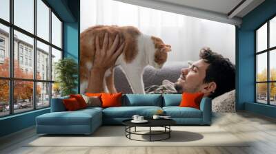 vertical composition. young man lying on the sofa and brown and white cat, interact under the window 2 Wall mural