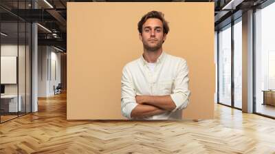 Young handsome Caucasian man over an isolated background, with arms crossed and looking forward. Wall mural