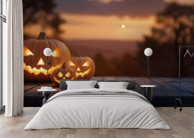 Two carved pumpkins with glowing faces on a wooden surface, with a blurred sunset landscape in the background Wall mural