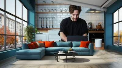 Happy curly hair man sitting in kitchen, using app with tablet computer, surfing on internet	
 Wall mural