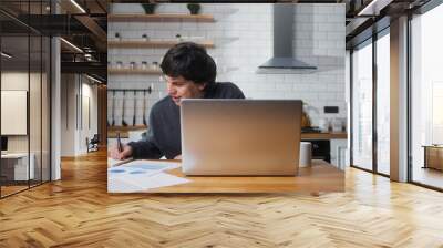 Smiling young university student sitting in the kitchen at home, looking laptop computer, studying, taking notes. Male student researching, study at home.	
 Wall mural