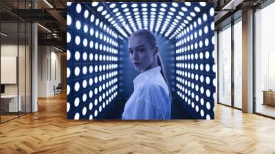 A young woman with a focused expression, positioned centrally. She is surrounded by a tunnel-like structure adorned with rows of illuminated circular lights.  Wall mural