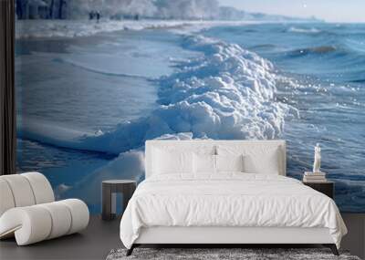 Snowy beach with gentle waves and trees along the coast under bright Winter sunlight Wall mural