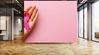 Hand holding breast cancer awareness symbol, isolated on pink background. National Breast Cancer Awareness Month, top view  Wall mural