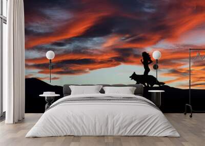 Silhouette of a woman running with dog in the landscape at sunset. Nature and sport. Wall mural