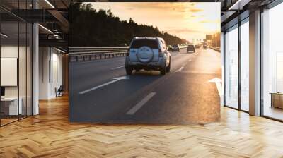 Cars in motion blur on highway during sunset. big road with metal safety barrier or rail under the cloudy blue sky and yellow and orange sun Wall mural