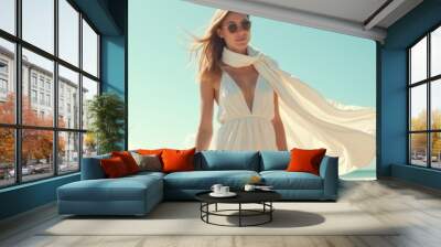 A confident woman walks along a sunny beach, exuding elegance in a flowing white dress, perfect for fashion, lifestyle, or travel marketing. Wall mural