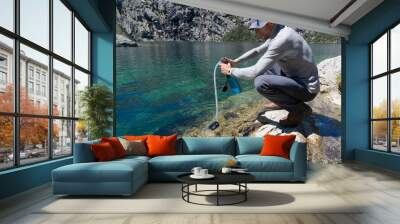 male hiker in a gray jersey and hat filtering drinking water from a turquoise mountain lake in the Cordillera Blanca in Peru Wall mural