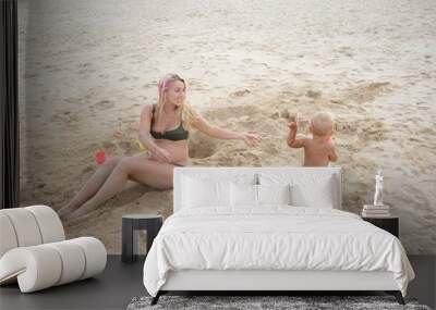 baby and pregnant her mother playing with sand on sea shore Wall mural