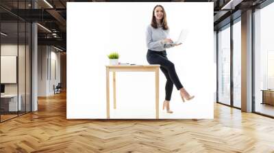 A girl in a good mood is sitting on a table and typing on a computer on a white background Wall mural