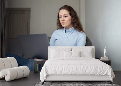 A girl in a shirt and jeans works at a computer at home Wall mural