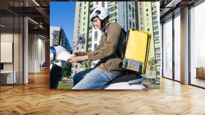 A man with a yellow courier bag sits on a scooter before going to a client. Online ordering of food from restaurants Wall mural