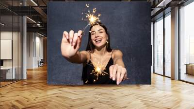 Portrait of a beautiful brunette in a black dress with sparklers. Wall mural