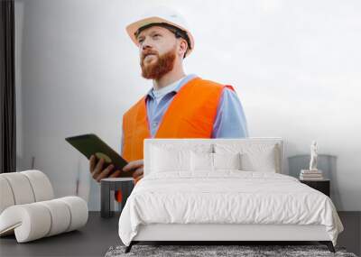 Portrait of a happy engineer in a white helmet and orange vest. A man writes data to a tablet against the background of a power plant Wall mural