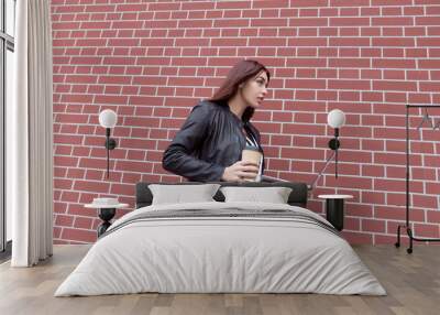 Red-haired girl in a black leather jacket works at the laptop against a red brick wall Wall mural