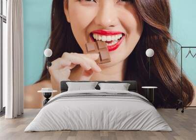 Attractive young asian woman eating chocolate, closeup Wall mural